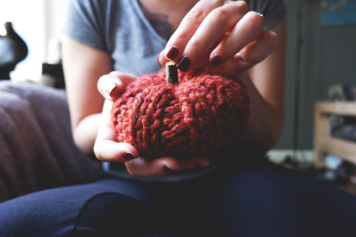 Small orange knit pumpkin in woman's hands.